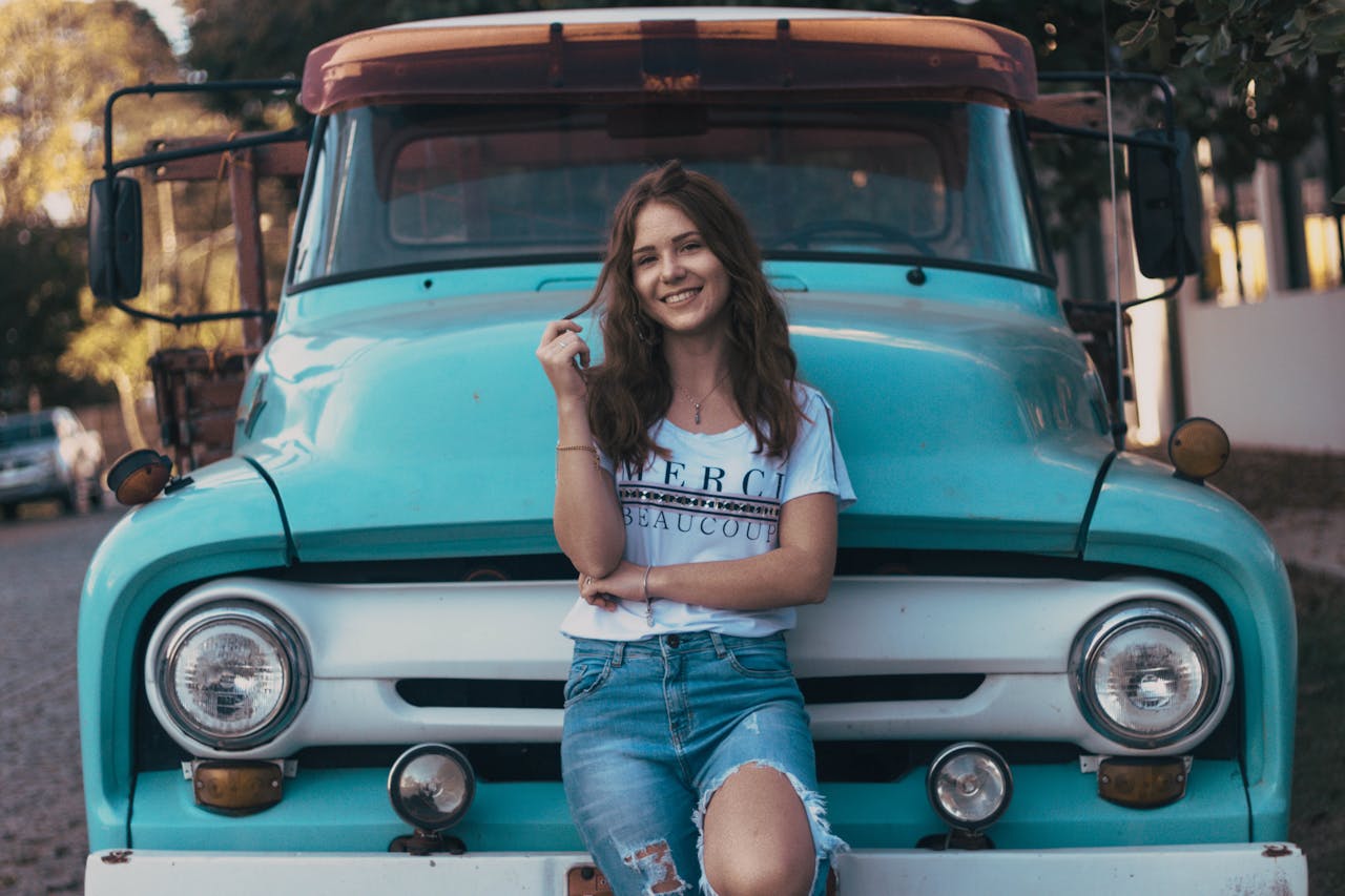 services-03 Happy young woman posing in front of classic retro truck on a sunny day outdoors.